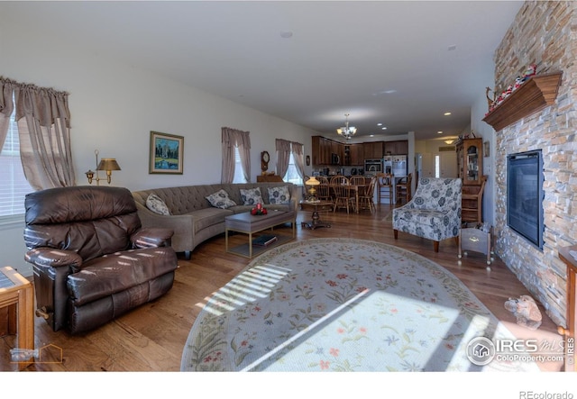 living room with a stone fireplace, a chandelier, and light wood-style floors