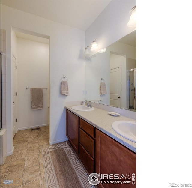 bathroom with baseboards, double vanity, a stall shower, and a sink