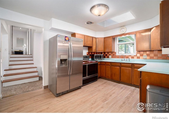 kitchen featuring light wood-type flooring, decorative backsplash, appliances with stainless steel finishes, and sink