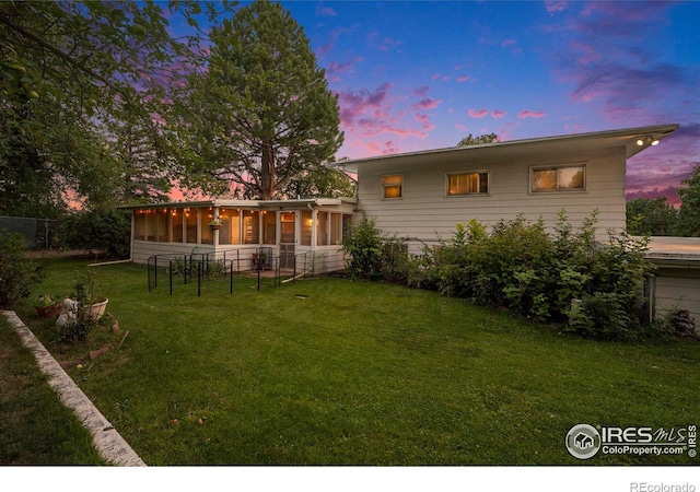 back house at dusk with a sunroom and a lawn