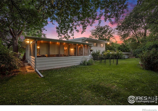 back house at dusk featuring a lawn