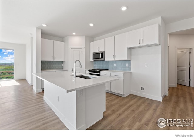 kitchen with decorative backsplash, a center island with sink, white cabinetry, and sink