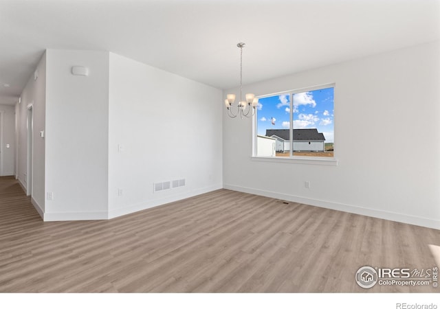 empty room featuring light wood-type flooring and a chandelier