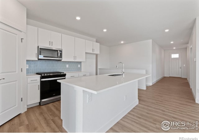 kitchen featuring stainless steel appliances, white cabinetry, a center island with sink, and sink