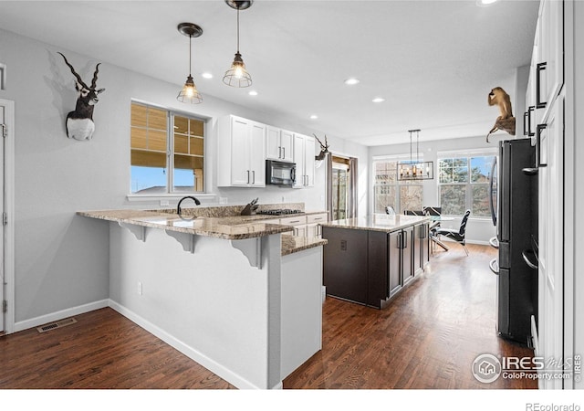 kitchen featuring appliances with stainless steel finishes, hanging light fixtures, a center island, light stone countertops, and white cabinets