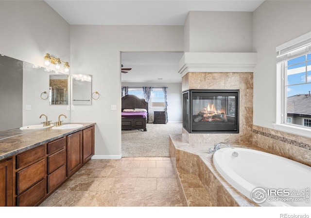 bathroom with a multi sided fireplace, plenty of natural light, tiled bath, and vanity