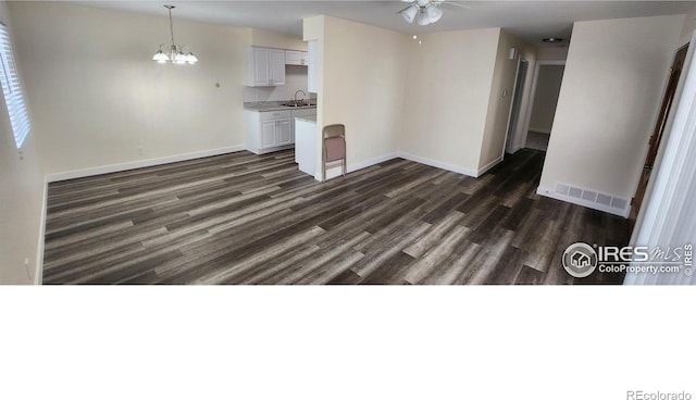 unfurnished living room featuring dark hardwood / wood-style flooring, sink, and ceiling fan with notable chandelier