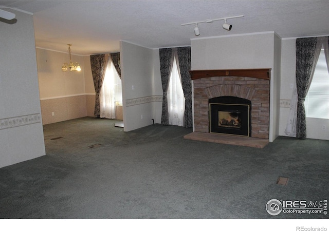 unfurnished living room with carpet, ornamental molding, a fireplace, a textured ceiling, and a chandelier