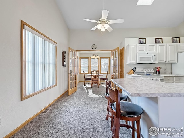 kitchen with white cabinetry, french doors, light colored carpet, white appliances, and a breakfast bar area