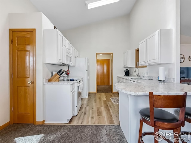 kitchen with a breakfast bar, white appliances, sink, kitchen peninsula, and white cabinetry