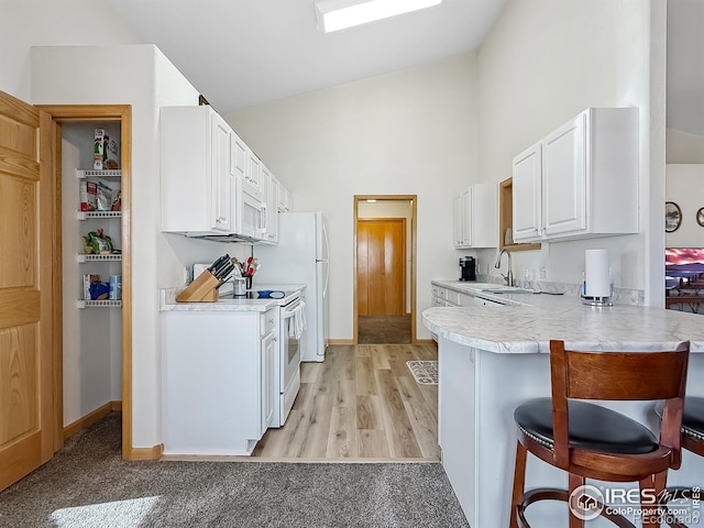 kitchen featuring white cabinetry, sink, kitchen peninsula, white appliances, and a breakfast bar area