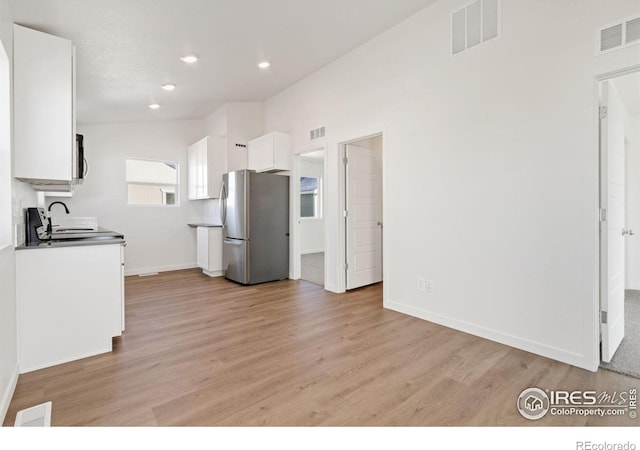 kitchen featuring stove, sink, light wood-type flooring, white cabinetry, and stainless steel refrigerator