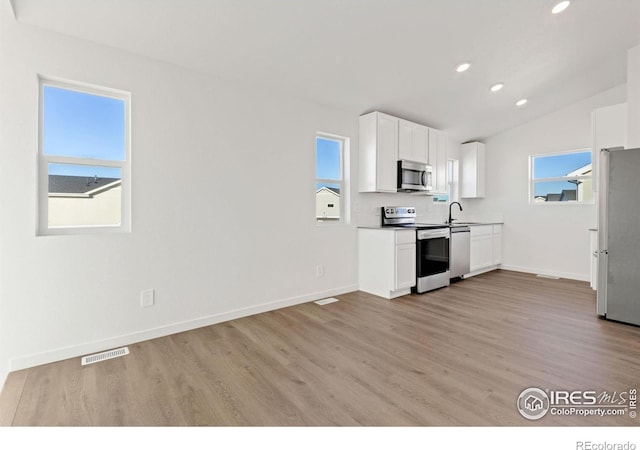 kitchen featuring appliances with stainless steel finishes, sink, light hardwood / wood-style flooring, white cabinetry, and lofted ceiling