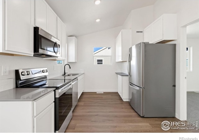 kitchen with sink, appliances with stainless steel finishes, vaulted ceiling, white cabinets, and light wood-type flooring