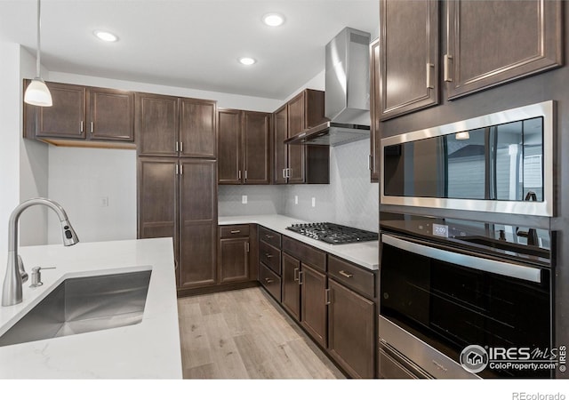 kitchen featuring hanging light fixtures, sink, wall chimney range hood, decorative backsplash, and stainless steel appliances