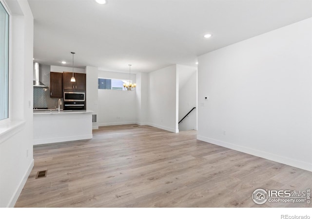 unfurnished living room with sink, light hardwood / wood-style flooring, and an inviting chandelier