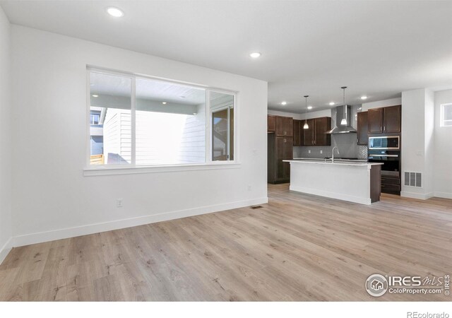 kitchen with appliances with stainless steel finishes, sink, tasteful backsplash, wall chimney range hood, and light hardwood / wood-style floors