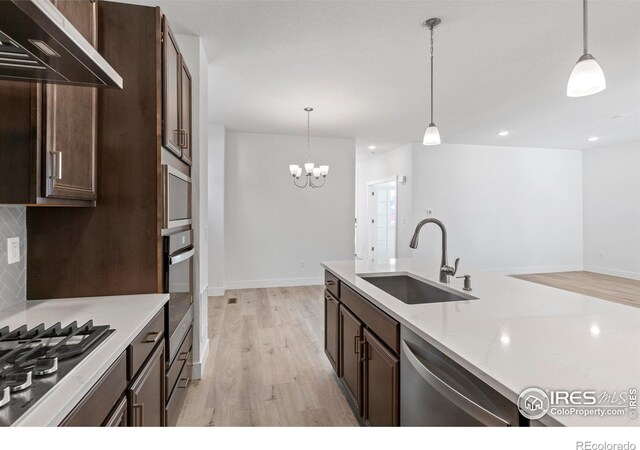 kitchen with light stone countertops, pendant lighting, wall chimney exhaust hood, stainless steel appliances, and sink