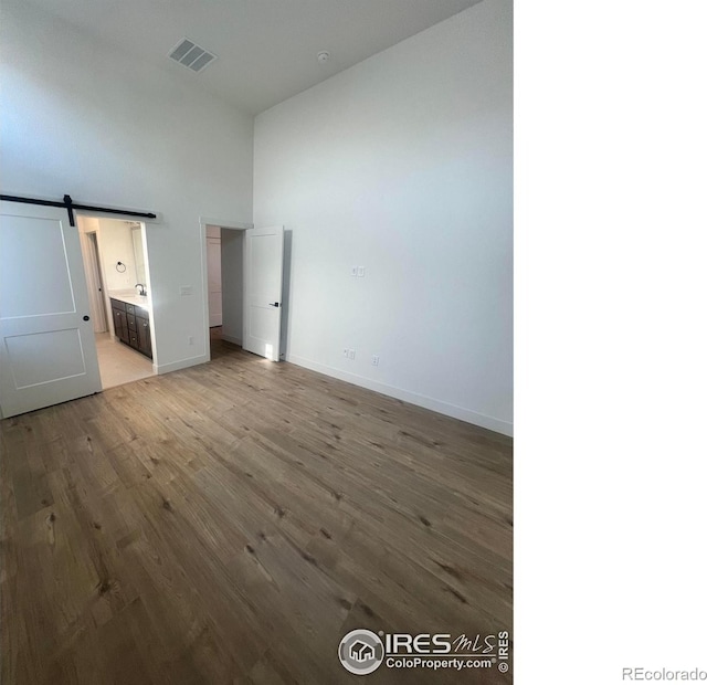 unfurnished bedroom featuring hardwood / wood-style flooring, ensuite bathroom, a barn door, and a towering ceiling