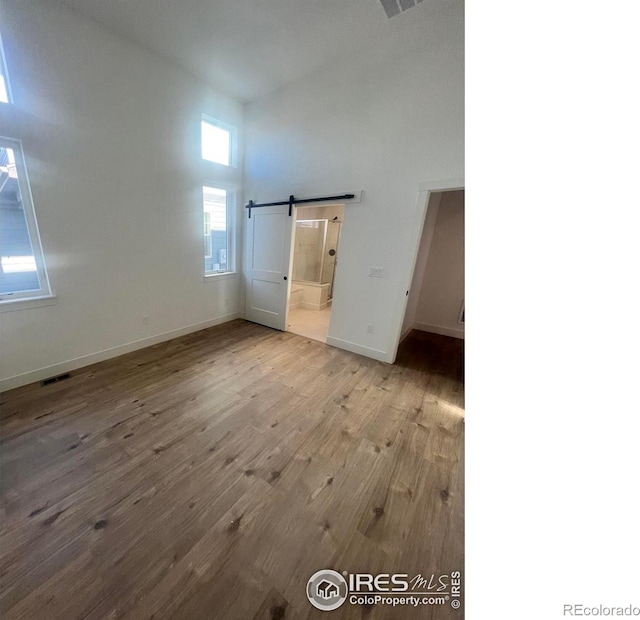 unfurnished bedroom featuring a towering ceiling, light hardwood / wood-style flooring, and a barn door