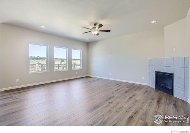 unfurnished living room with ceiling fan, a tile fireplace, and light hardwood / wood-style flooring