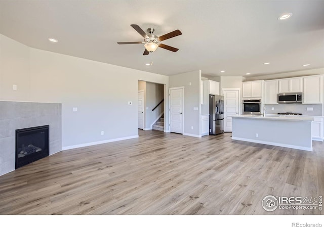 unfurnished living room with a fireplace, ceiling fan, and light hardwood / wood-style flooring