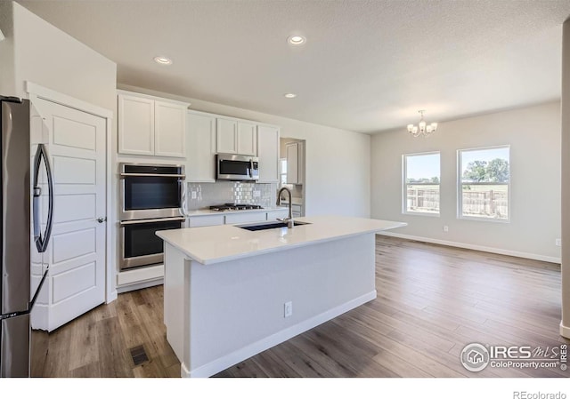 kitchen with stainless steel appliances, white cabinetry, a kitchen island with sink, and sink