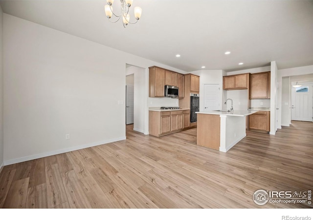 kitchen featuring a kitchen island with sink, decorative light fixtures, light wood-type flooring, and appliances with stainless steel finishes