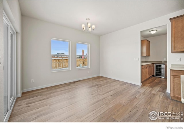 unfurnished dining area with wine cooler, a chandelier, and light hardwood / wood-style flooring