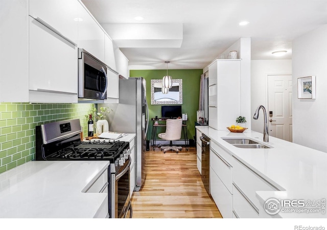 kitchen with appliances with stainless steel finishes, tasteful backsplash, sink, white cabinets, and hanging light fixtures