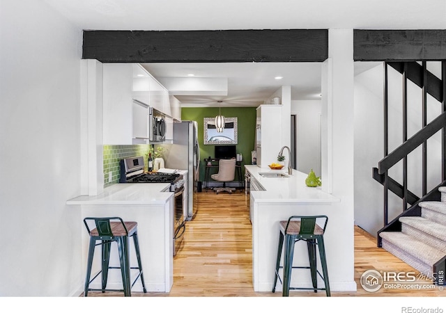 kitchen featuring a breakfast bar, hanging light fixtures, sink, appliances with stainless steel finishes, and white cabinetry