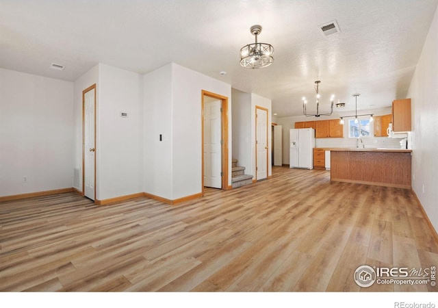 unfurnished living room featuring sink, light hardwood / wood-style flooring, a textured ceiling, and a notable chandelier