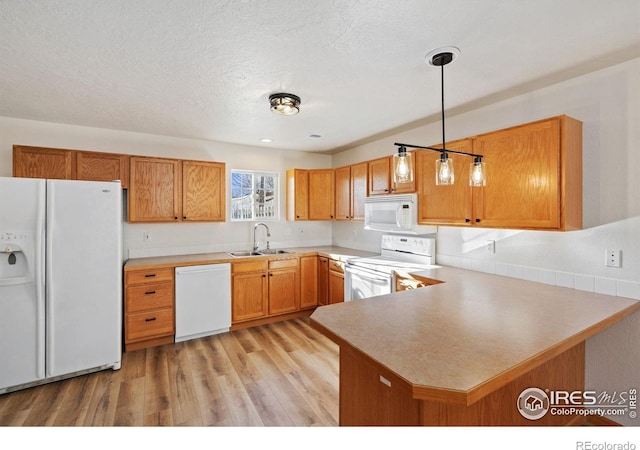 kitchen featuring pendant lighting, white appliances, sink, light hardwood / wood-style flooring, and kitchen peninsula