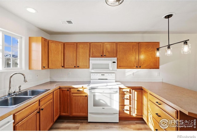 kitchen with sink, kitchen peninsula, decorative light fixtures, white appliances, and light wood-type flooring