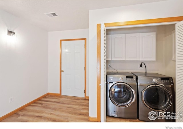 clothes washing area with washer and dryer, cabinets, and light hardwood / wood-style flooring