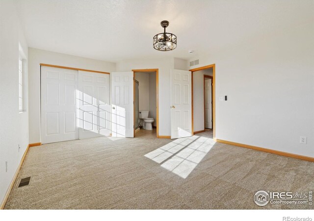 unfurnished bedroom with a chandelier, light colored carpet, connected bathroom, and a closet