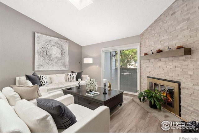 living area with vaulted ceiling with skylight, a fireplace, and wood finished floors