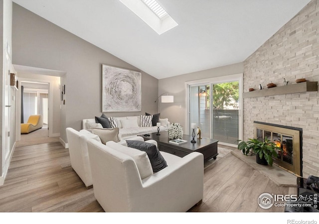 living room with a skylight, a large fireplace, high vaulted ceiling, and light wood-style flooring