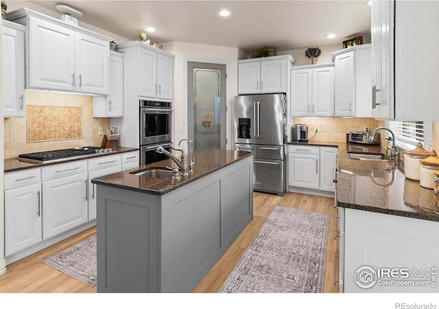 kitchen featuring white cabinetry, sink, dark stone countertops, a kitchen island with sink, and stainless steel appliances