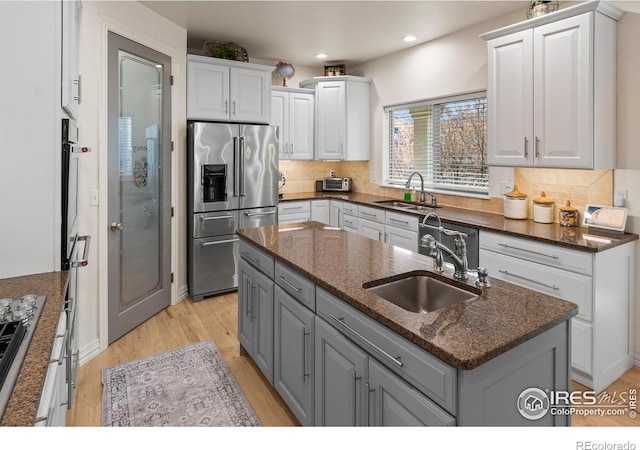 kitchen featuring sink, an island with sink, dark stone counters, and appliances with stainless steel finishes