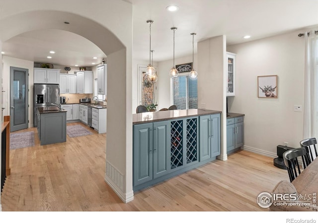 kitchen with appliances with stainless steel finishes, white cabinetry, hanging light fixtures, kitchen peninsula, and light hardwood / wood-style flooring