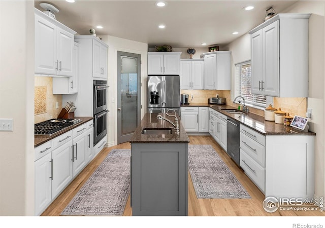 kitchen with an island with sink, appliances with stainless steel finishes, sink, and white cabinets