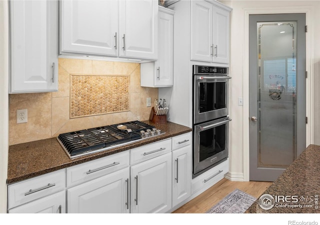 kitchen with white cabinetry, appliances with stainless steel finishes, light hardwood / wood-style floors, and dark stone counters