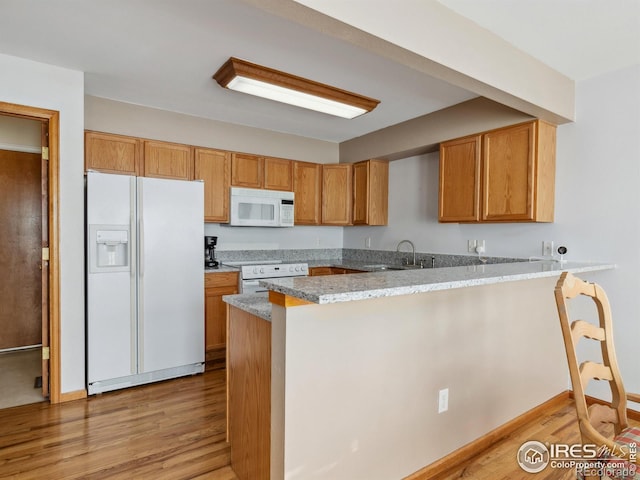 kitchen with white appliances, sink, light hardwood / wood-style floors, light stone counters, and kitchen peninsula