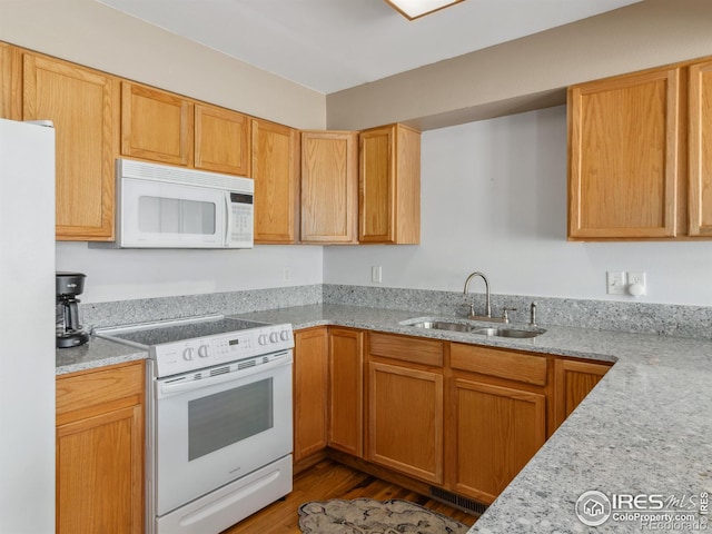 kitchen with hardwood / wood-style flooring, light stone countertops, white appliances, and sink