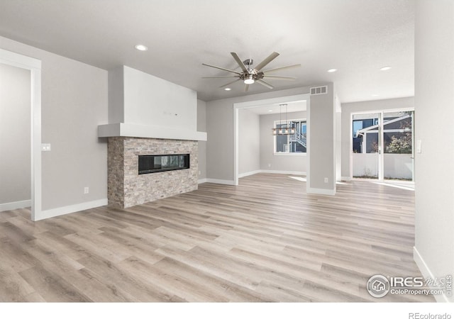 unfurnished living room featuring light hardwood / wood-style flooring, ceiling fan with notable chandelier, and a fireplace