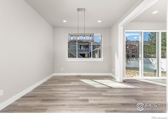 unfurnished dining area with an inviting chandelier and light wood-type flooring