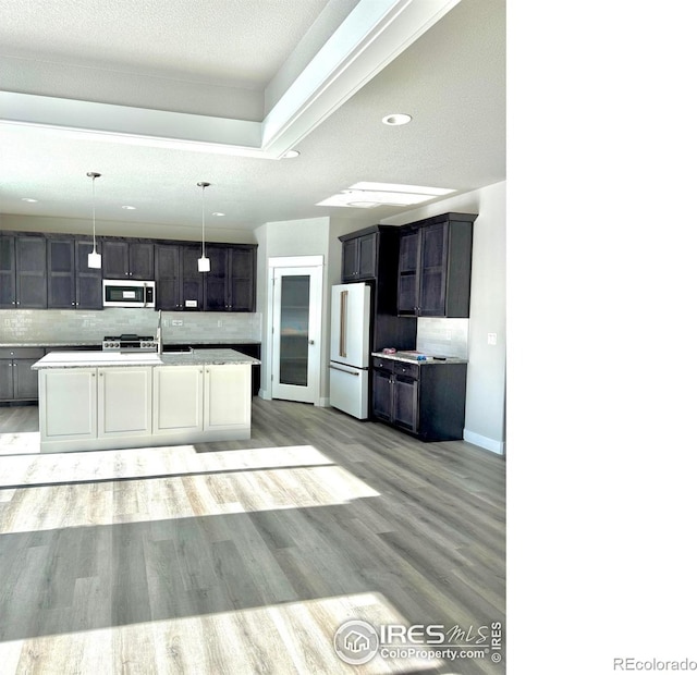 kitchen featuring hanging light fixtures, high end white refrigerator, a kitchen island with sink, and backsplash