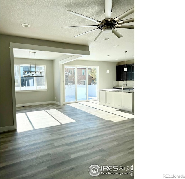 unfurnished living room featuring a healthy amount of sunlight, sink, light hardwood / wood-style flooring, and a textured ceiling