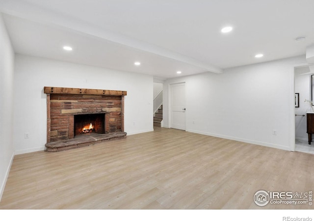 unfurnished living room featuring beam ceiling, light hardwood / wood-style floors, and a stone fireplace